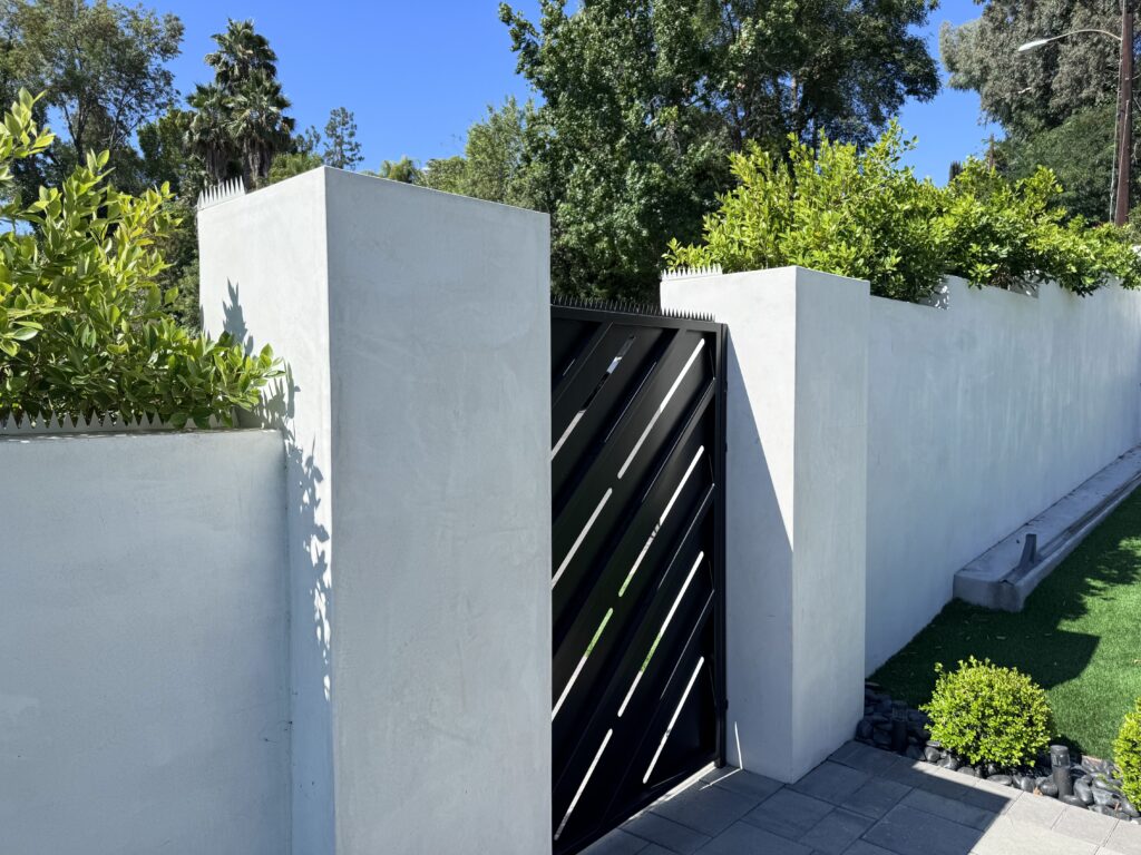 Portón moderno negro integrado en un muro blanco, con pinchos antiescalada a lo largo de la parte superior