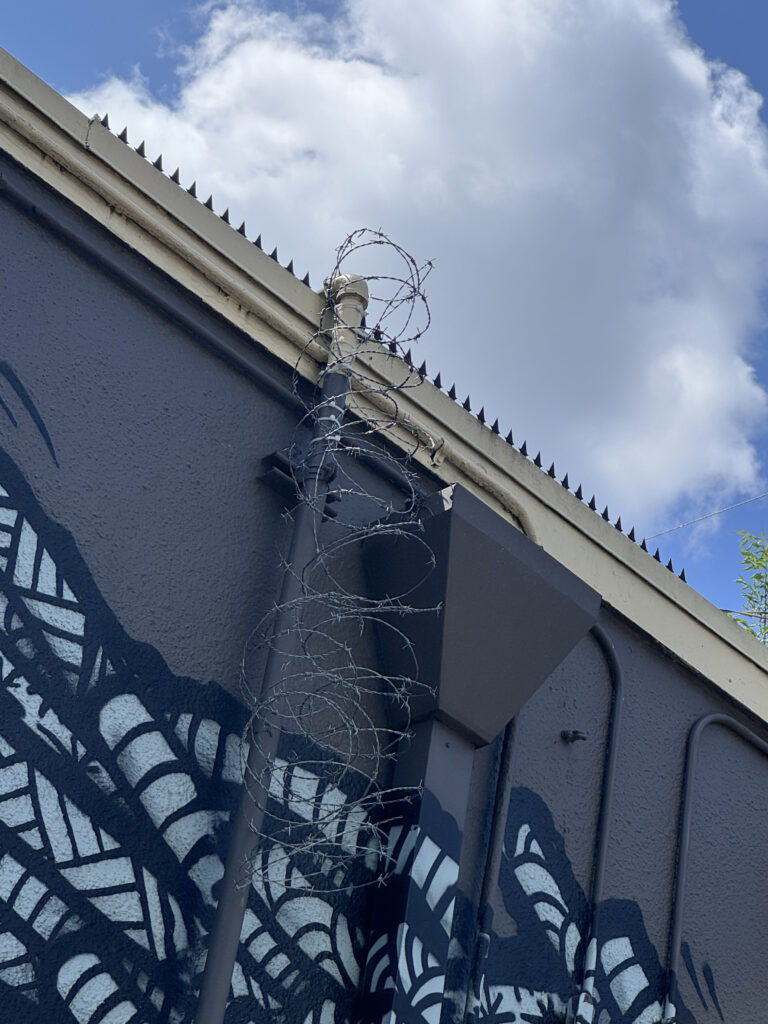 Gros plan des pics de sécurité sur la toiture et du fil concertina sur fond de ciel bleu