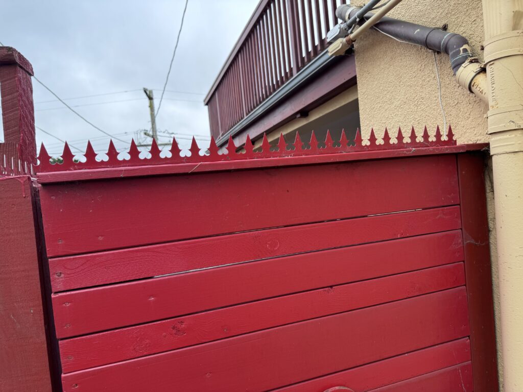 Primer plano de spikes de seguridad anti-escalada rojos instalados sobre una valla de madera roja.