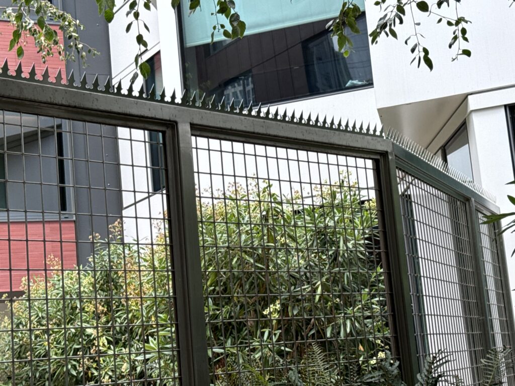 中庭の植物と集合住宅外観に沿って設置された、金属フェンス＋アンチクライムスパイク。