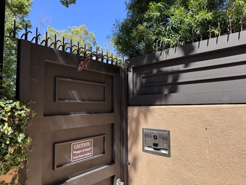 Entry gate and intercom panel beside a black fence topped with Classic Short Dual (Black) anti-climb spikes