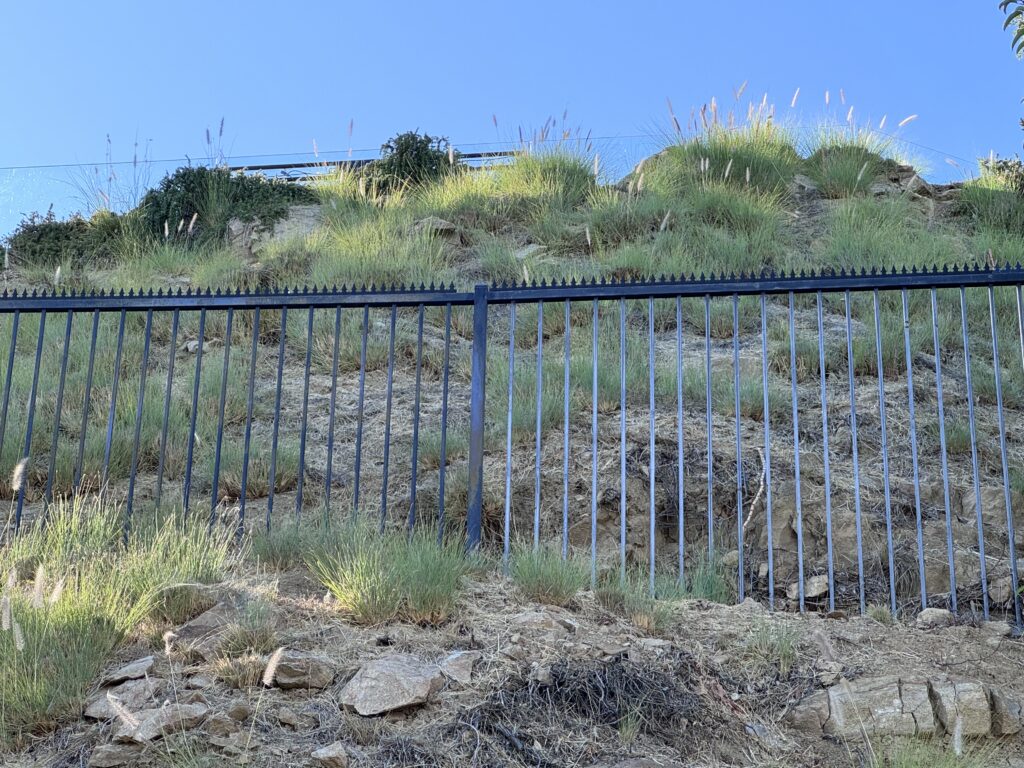 Long metal fence run on a hillside with Gothic (Black) anti-climb deterrent installed along the top.