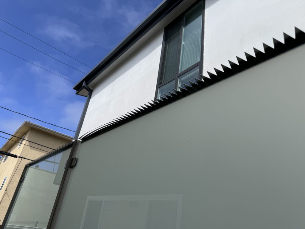 Vue latérale d’une maison moderne avec des pics de sécurité anti-escalade le long du sommet d’un mur d’intimité, sous un ciel bleu.