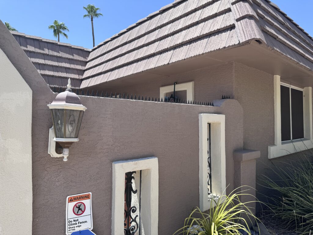 Stucco perimeter wall topped with Gothic anti-climb spikes under a clear Phoenix sky.