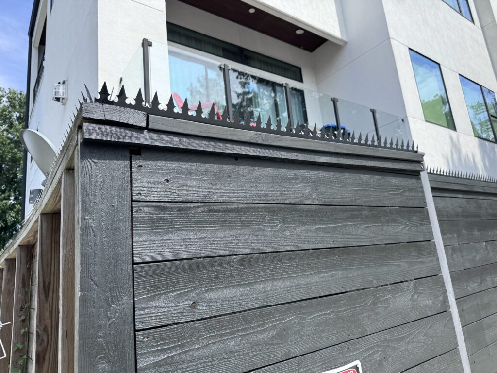 Detalhe de canto de uma cerca de madeira em tom carvão com a coroa Gothic preta ao lado de uma casa moderna em estuque, Stanford St, Houston.