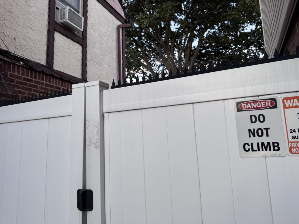 Low-profile black anti-climb spikes installed as a continuous crown on a white vinyl fence