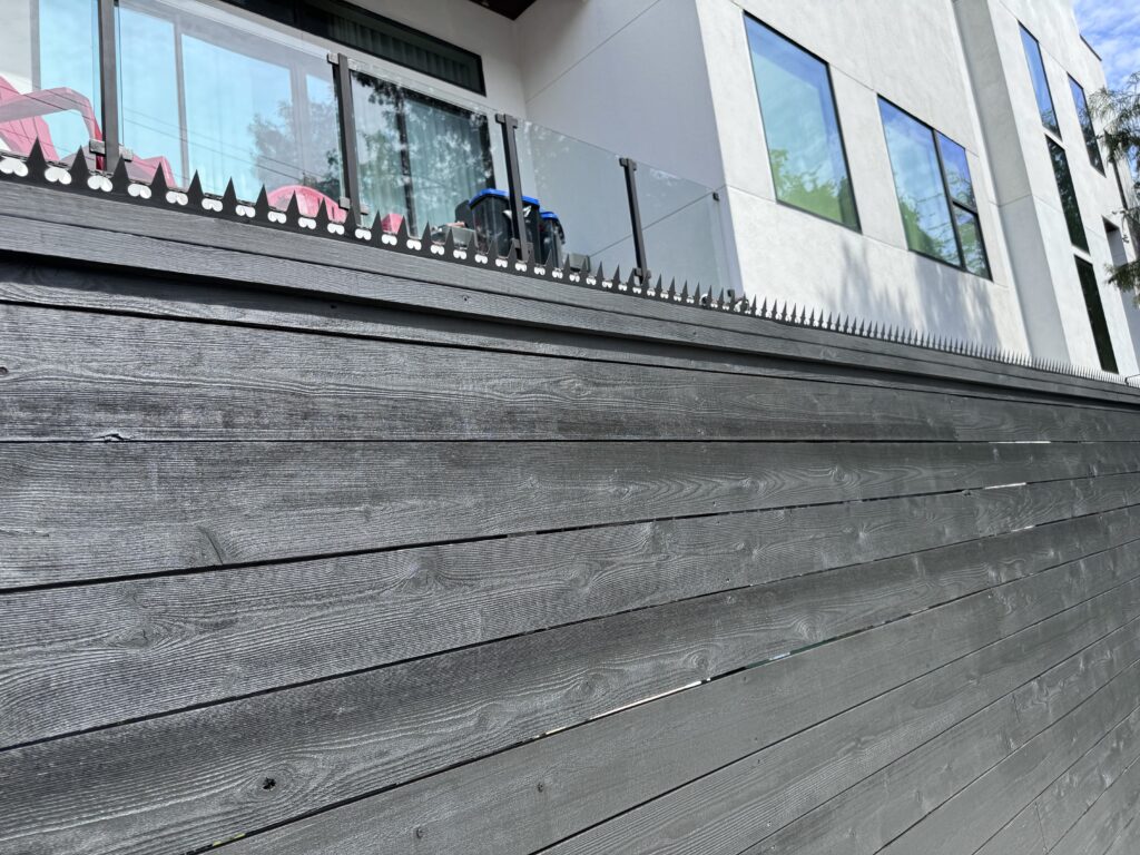 모던한 흰색 주택과 발코니 옆의 목재 펜스, 상단에 월담 방지 스파이크 설치.