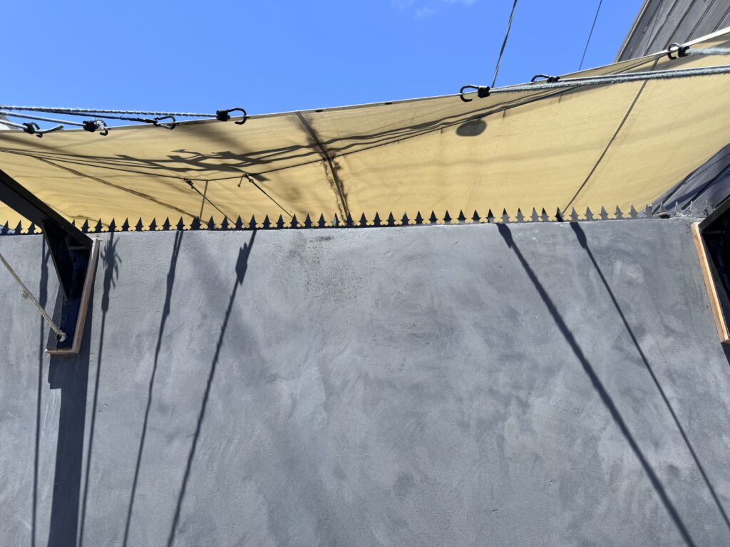 Durchgehender Gothic Anti-Climb-Deterrent entlang der Oberkante einer dunklen Putzwand.