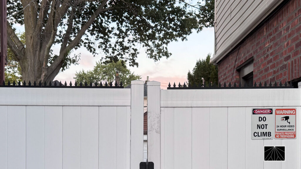 White vinyl privacy fence topped with anti-climb spikes, with “Do Not Climb” and surveillance warning signs.