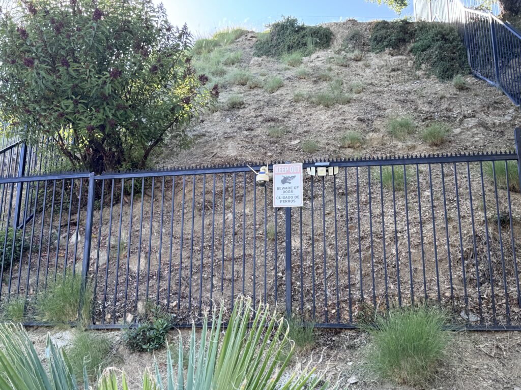 Clôture métallique avec panneau de sécurité et luminaires, surmontée d’un dissuasif anti-escalade Gothic (Black) sur une propriété en hillside.