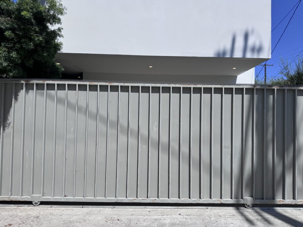 Portail en acier gris devant un bâtiment blanc, surmonté d’une rangée continue de pointes anti-escalade.