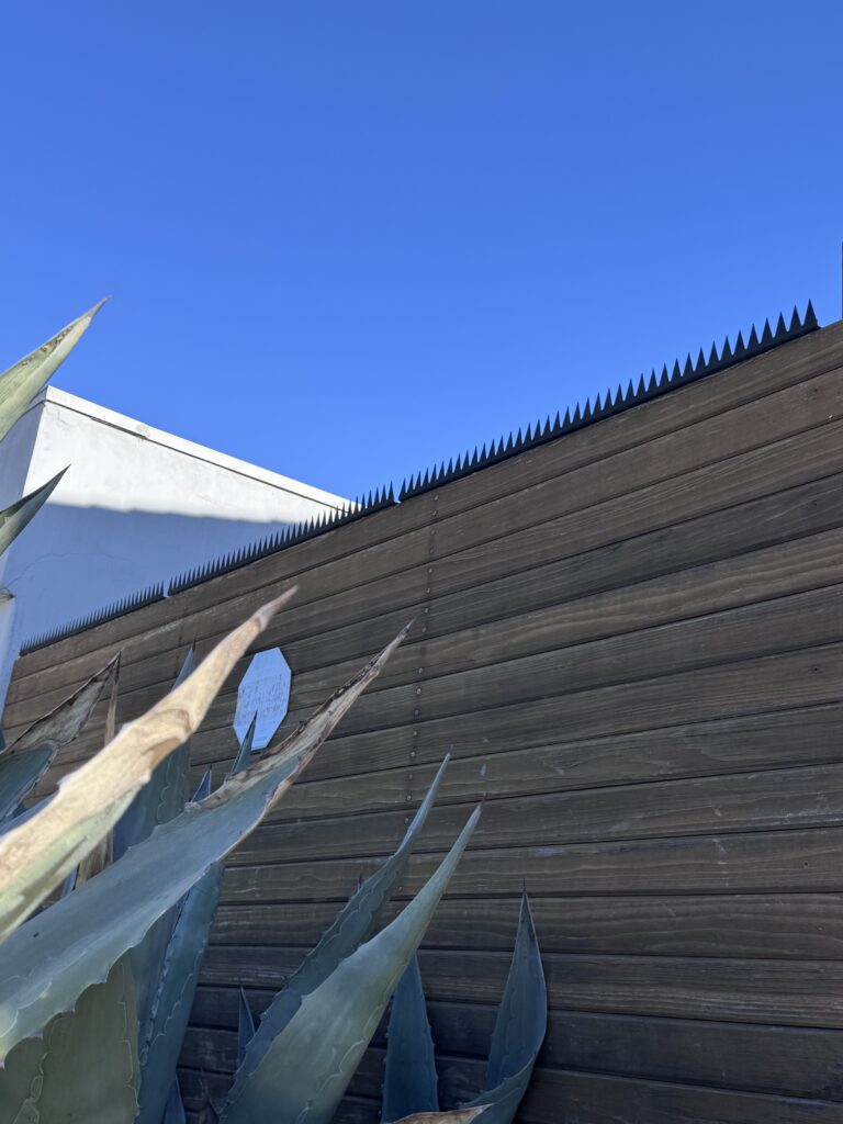 전경의 아가베 식재와 함께, 상단에 월담 방지 보안 스파이크가 설치된 다크 우드 프라이버시 펜스