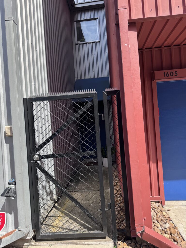 Portão chain-link com moldura preta e pontas de segurança no topo, entrada industrial.