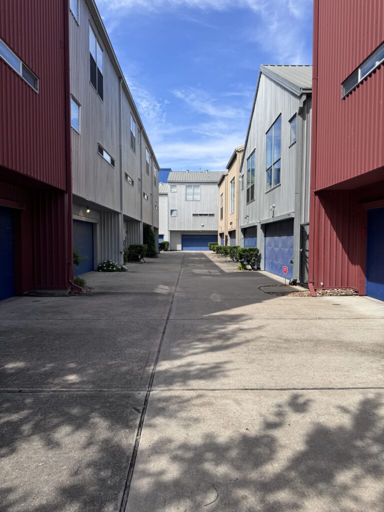 Portão de segurança chain-link com pontas no topo, ao lado de uma fachada de prédio em metal.