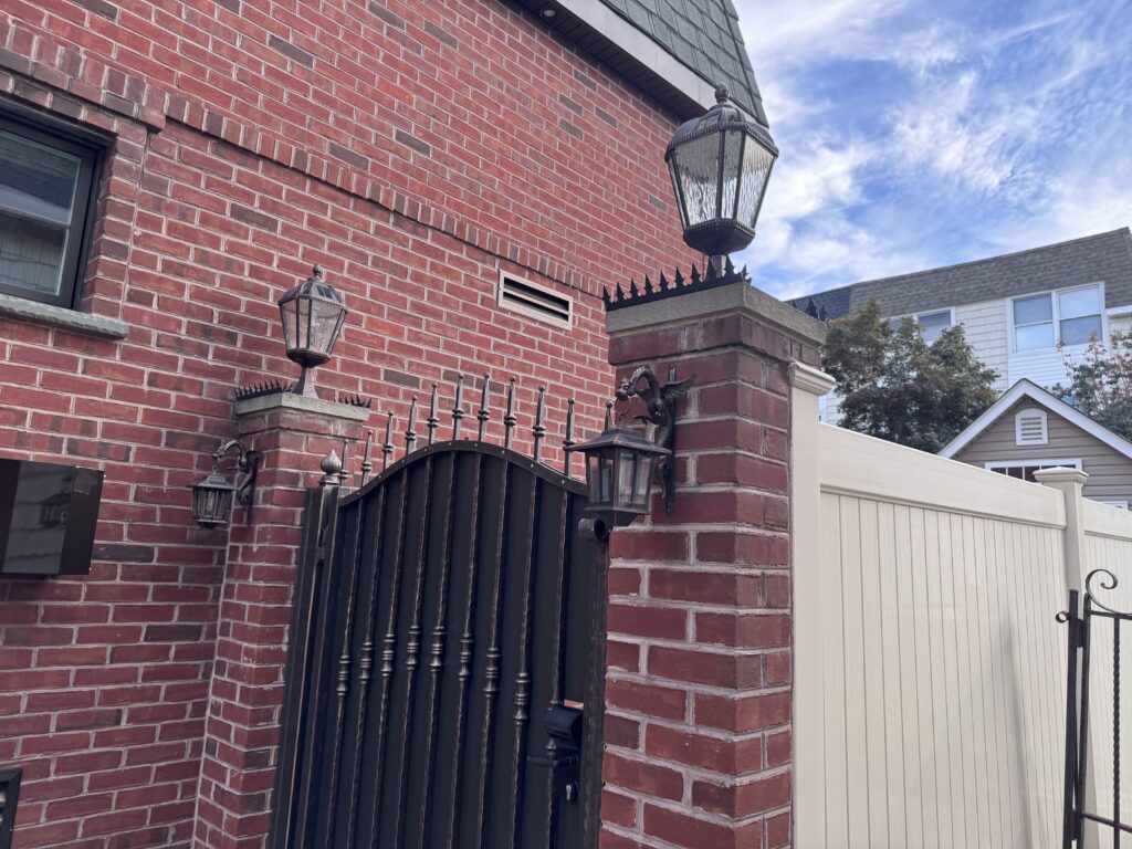 Close de um pilar de tijolo com lanterna e spikes anti-escalada acima de um portão metálico preto