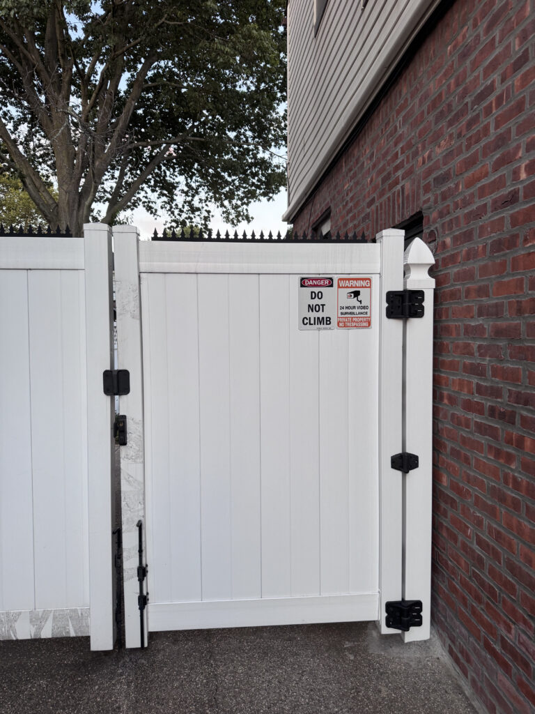 Señalización de advertencia en un portón de vinilo blanco junto con pinchos discretos para disuasión en capas